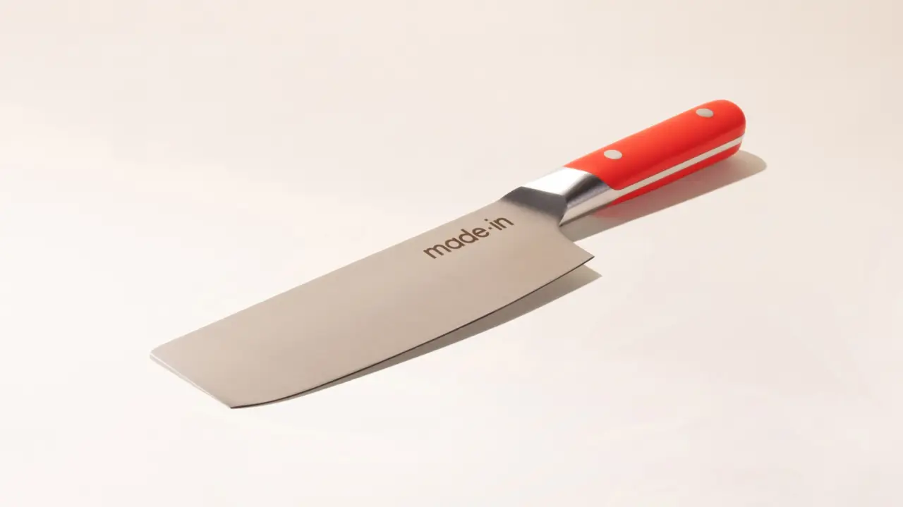 A chef's knife with a red and silver handle lies on a plain background.