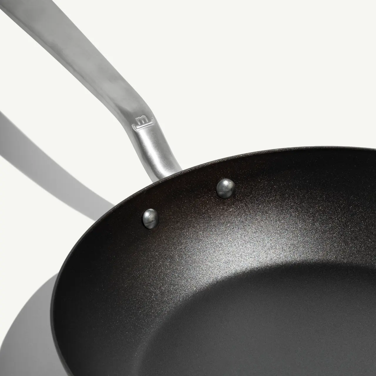 A sleek, black frying pan with a stainless steel handle is shown against a light background.
