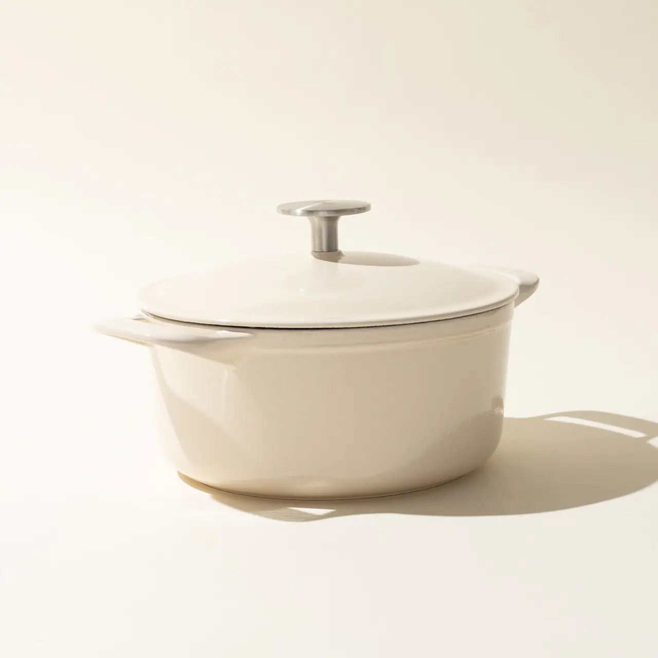A minimalist image featuring a antique white-colored saucepan with a lid against a light background, casting a soft shadow to the right.