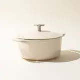 A minimalist image featuring a antique white-colored saucepan with a lid against a light background, casting a soft shadow to the right.