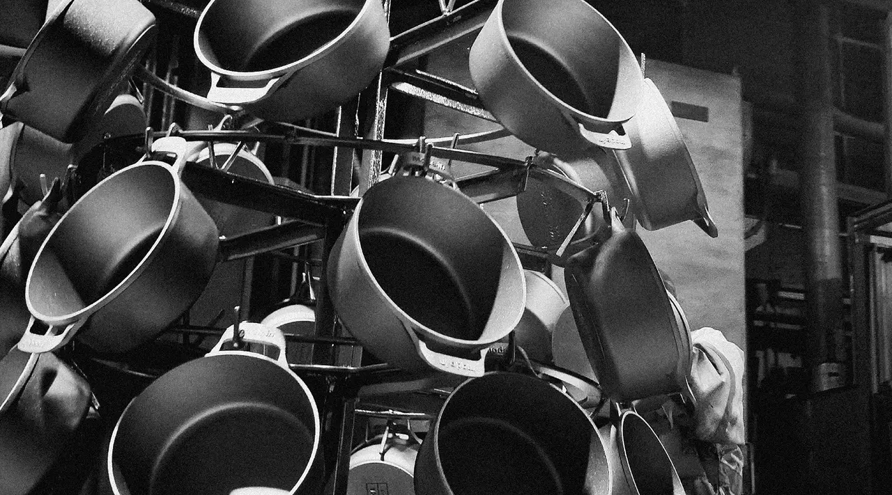 A collection of various sized frying pans hangs in disarray against a dimly lit background.