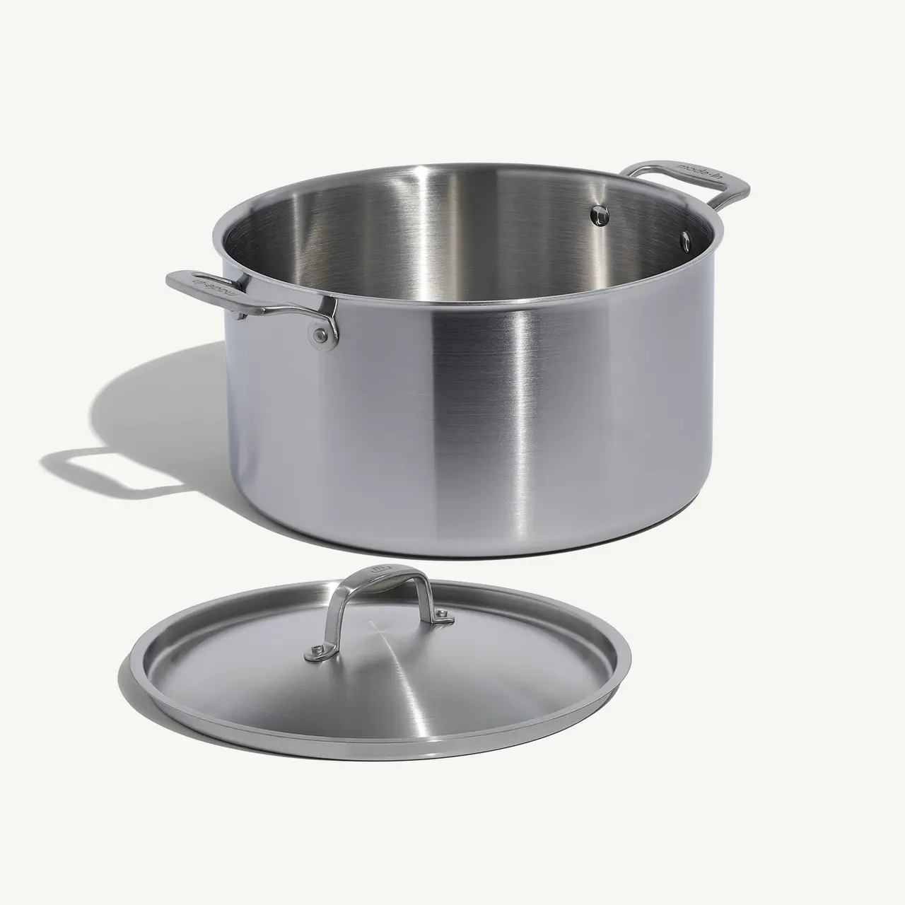 A stainless steel cooking pot sits next to its lid on a light background.