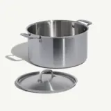 A stainless steel cooking pot sits next to its lid on a light background.