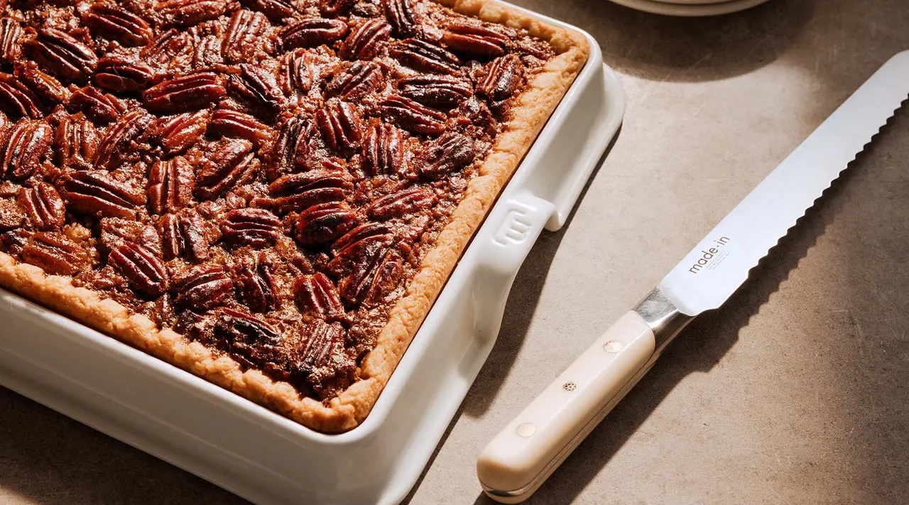 A freshly baked pecan pie sits next to a serrated knife on a kitchen counter, ready to be served.