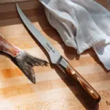 A carving knife lies next to a fish tail and a white cloth on a wooden cutting board.