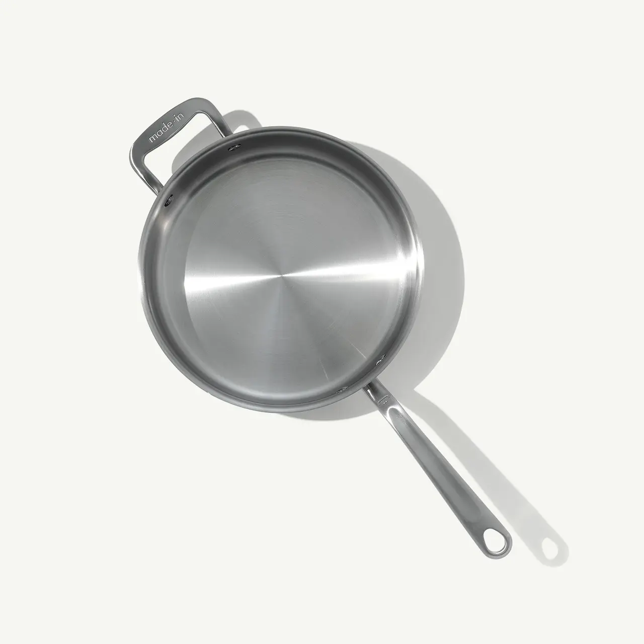 A stainless steel frying pan with a long handle is positioned against a plain background.