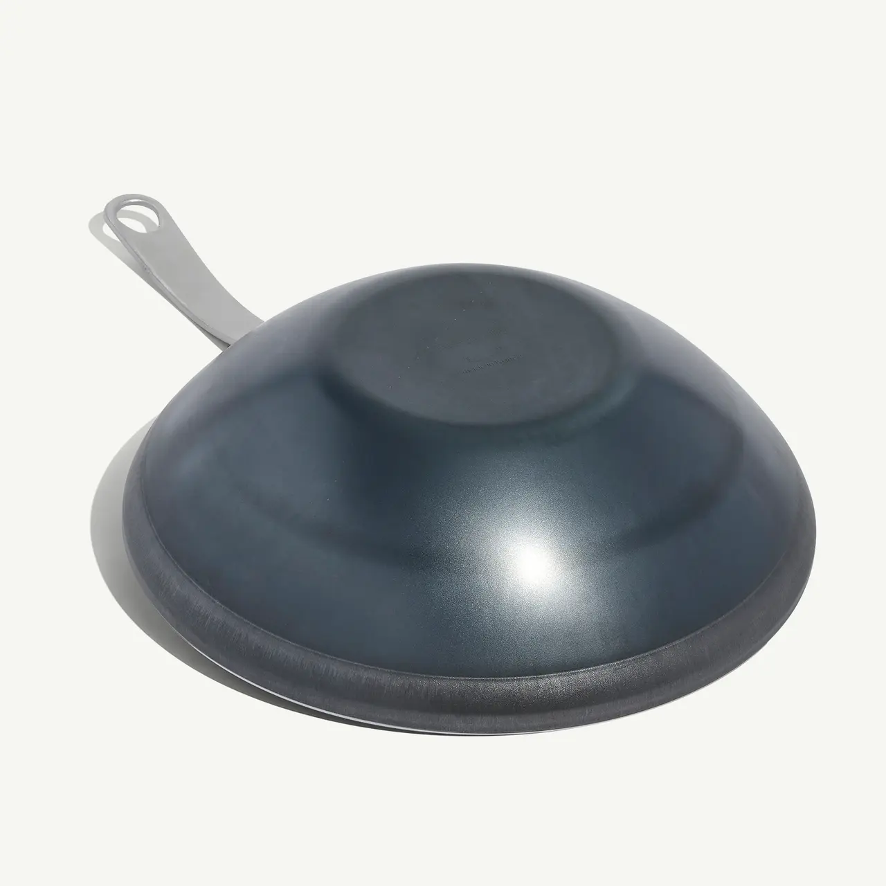 A black wok-style frying pan with a handle is shown against a light background.