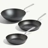 Three black cookware items are displayed, including a wok and two frying pans of varying sizes, all featuring shiny metal handles.