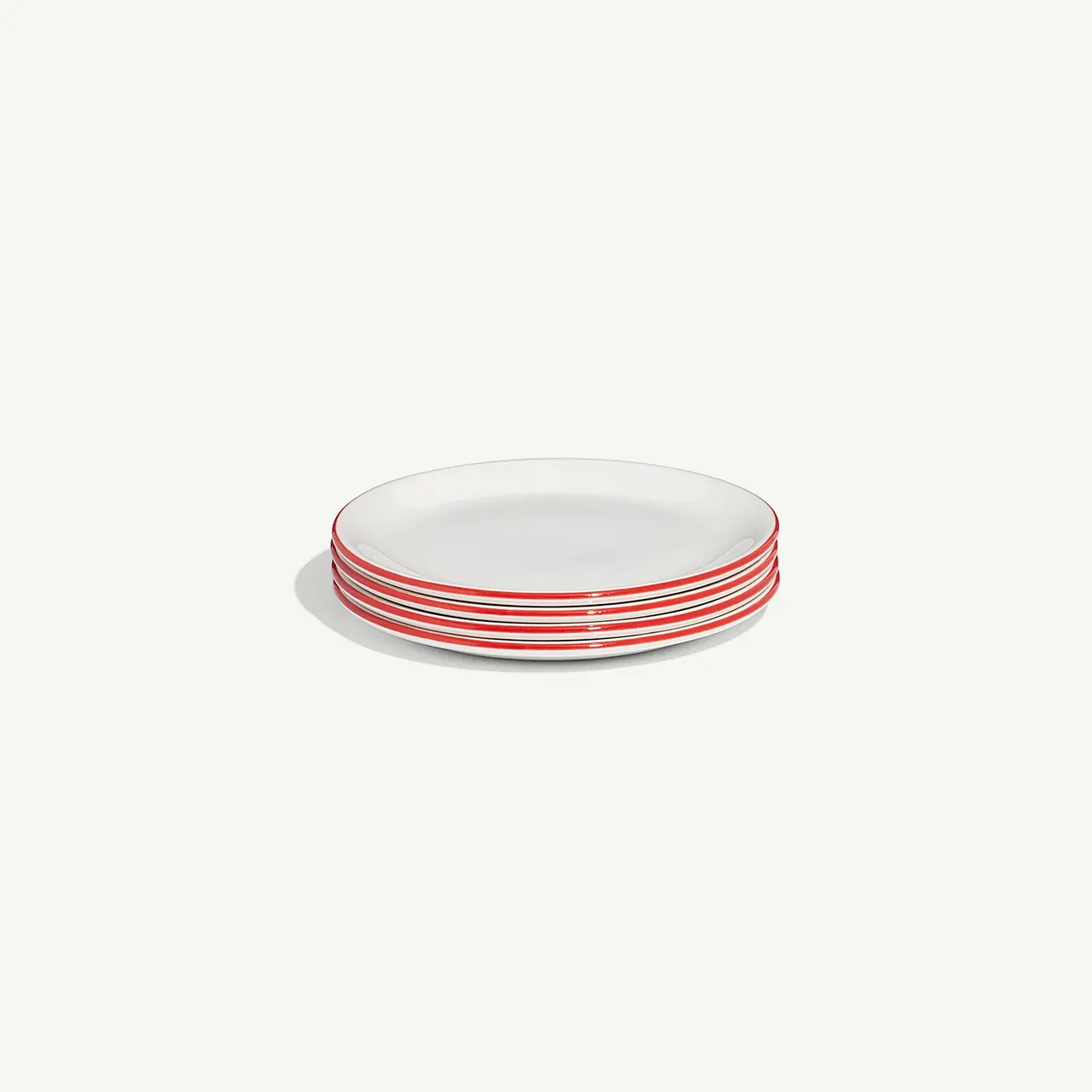 A stack of white plates with a red stripe around the rim sits on a plain background.