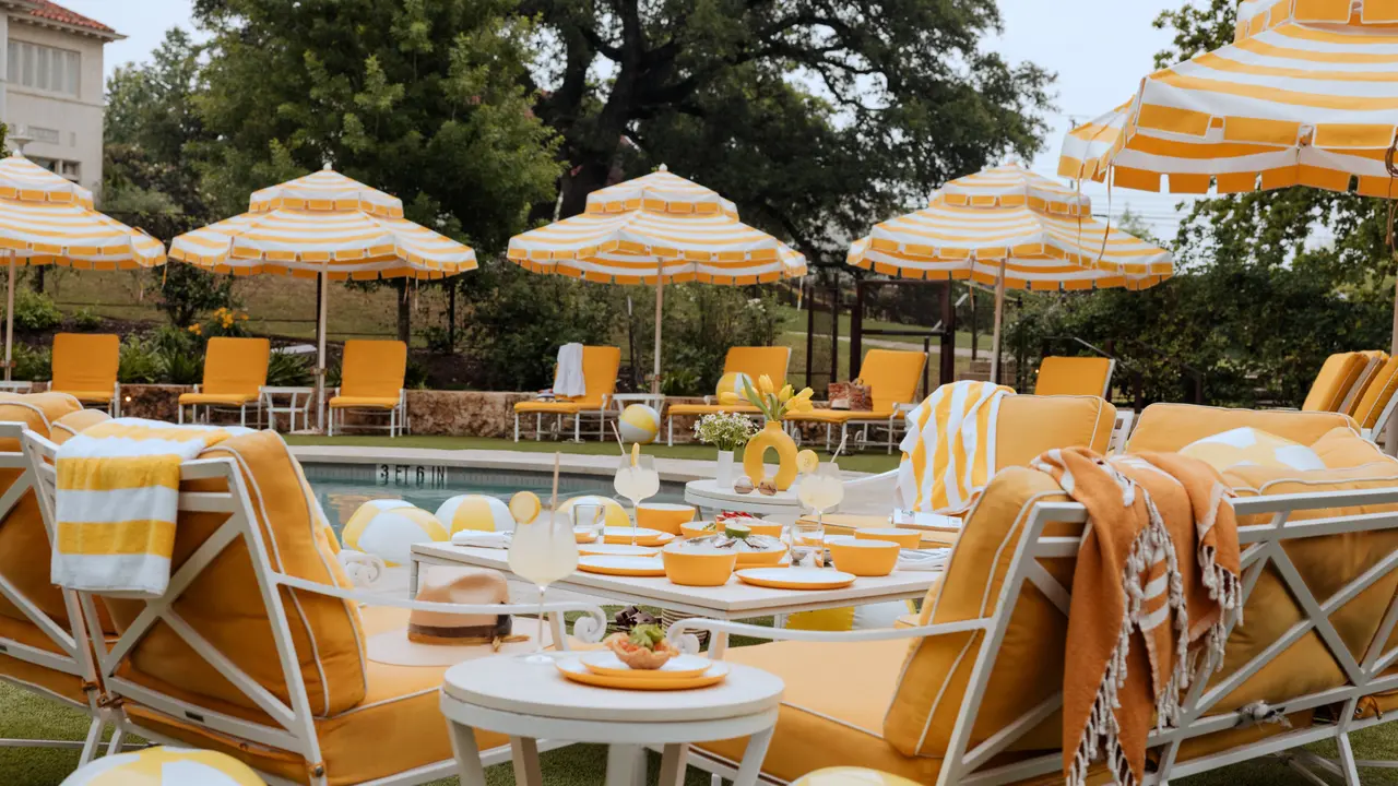 An outdoor dining area is set up with yellow and white striped umbrellas and matching sun loungers beside a swimming pool, ready for guests to enjoy.