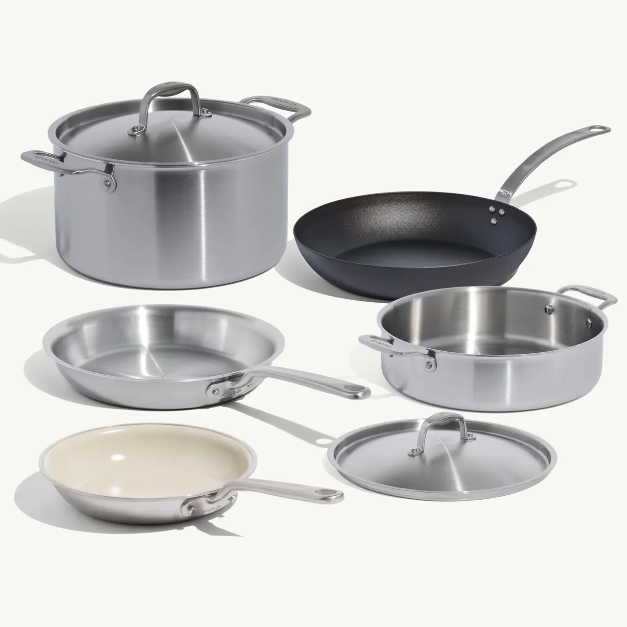 A variety of stainless steel cooking pots and pans, including a stockpot, frying pan, and saucier, arranged on a light background.