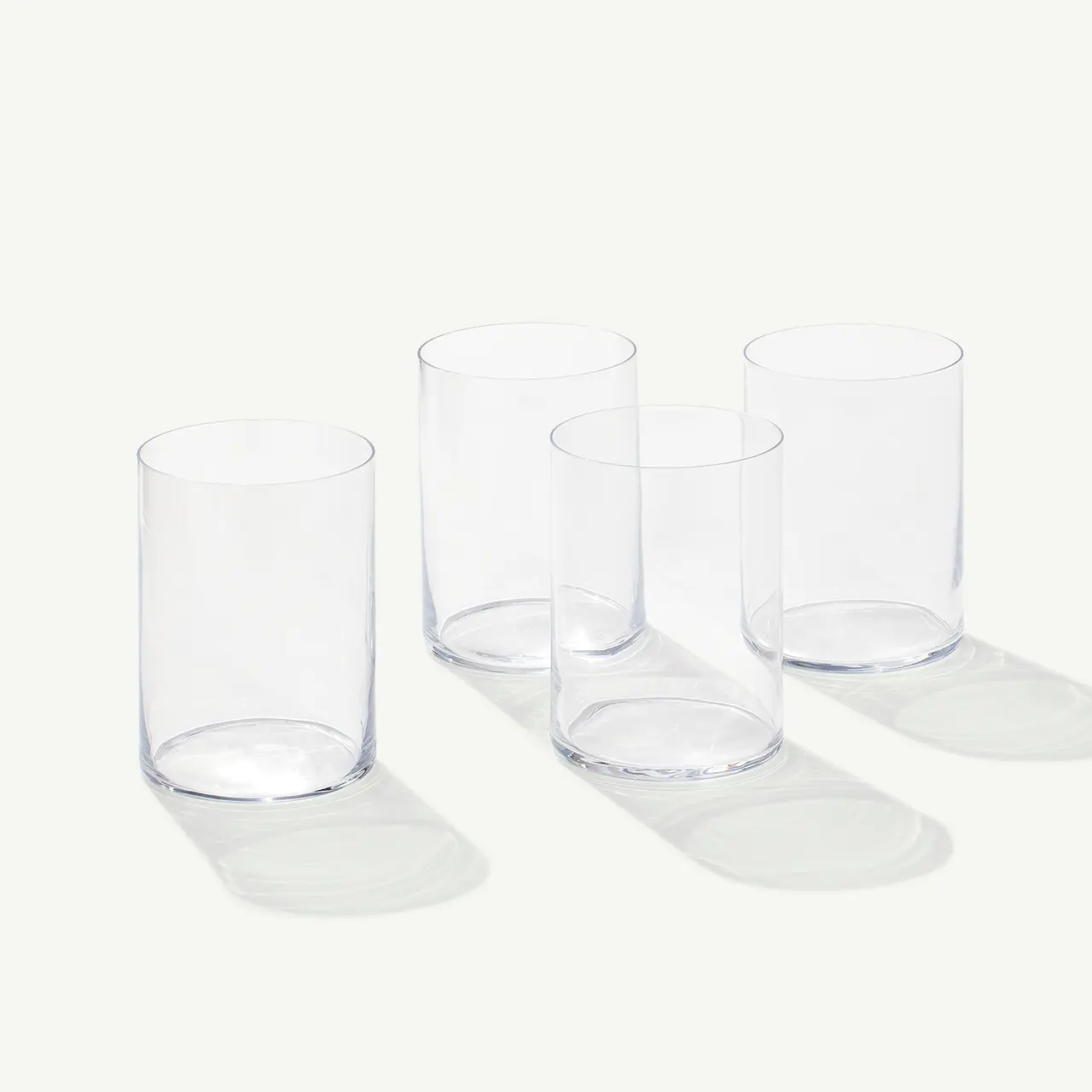 Four clear drinking glasses are arranged neatly on a light background, casting soft shadows.