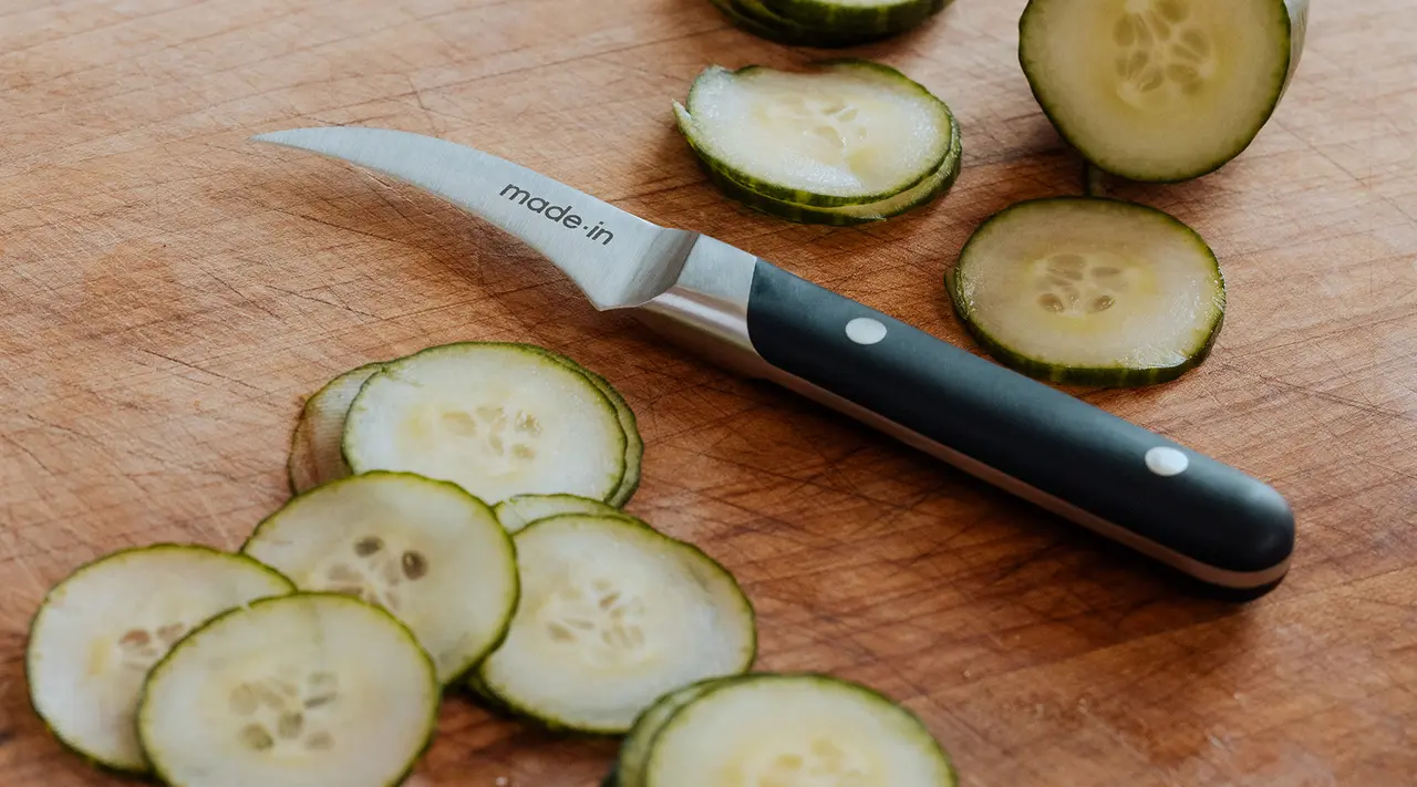 Sliced cucumbers lie next to a paring knife on a wooden cutting board.