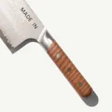 A polished kitchen knife with a textured blade and a wooden handle is displayed, featuring the text "MADE IN" on the blade.