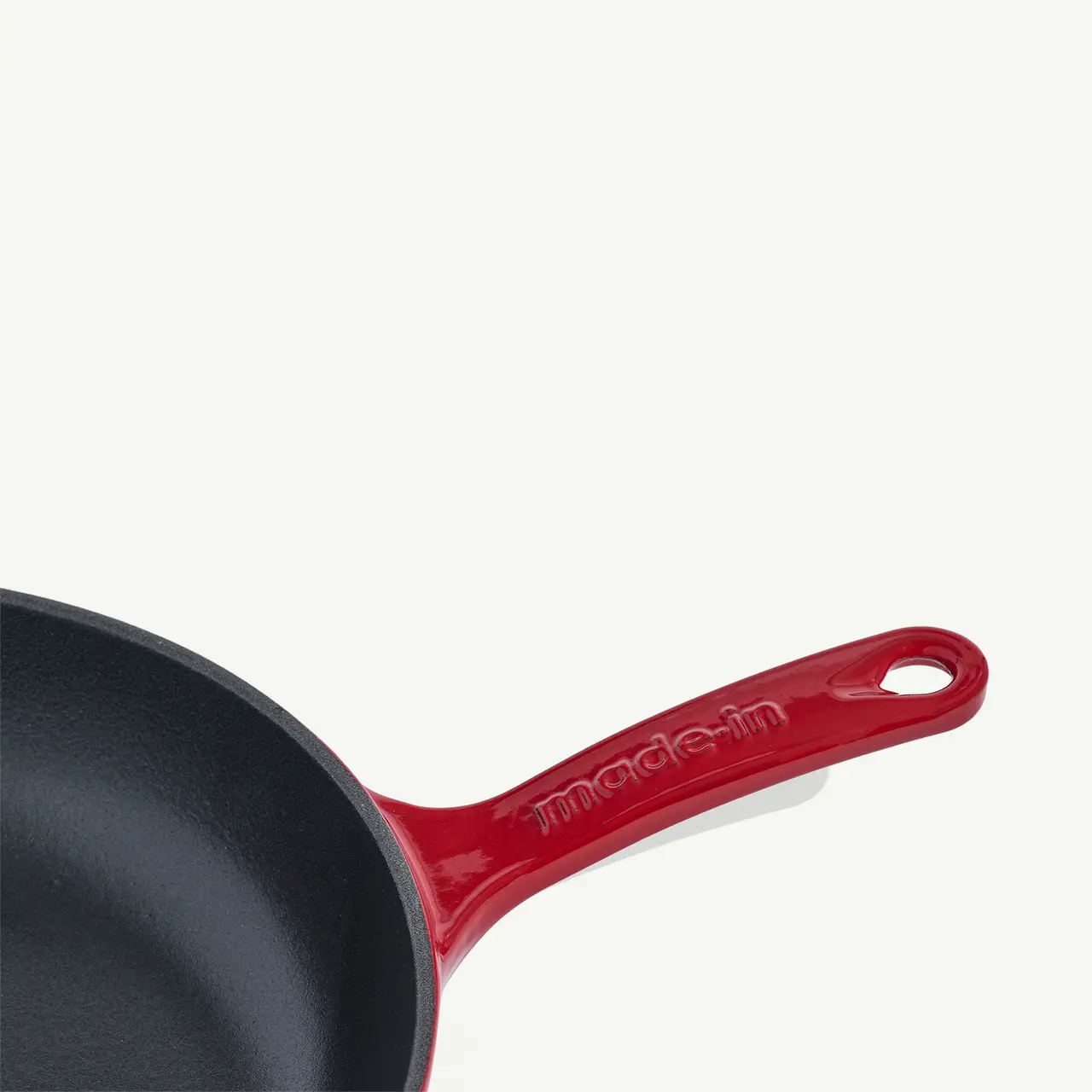 A black non-stick frying pan with a glossy red handle that has the text "made in" printed on it is shown against a white background.