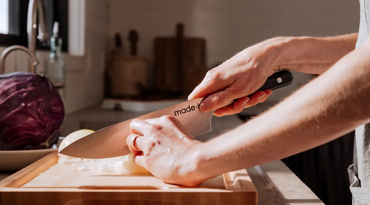 A person is slicing an onion on a wooden cutting board in a kitchen setting with a red cabbage also visible.