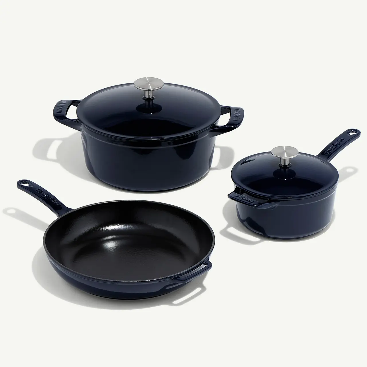 A set of navy blue cookware, including a skillet, a pot, and a saucepan with lids, is arranged on a light surface.