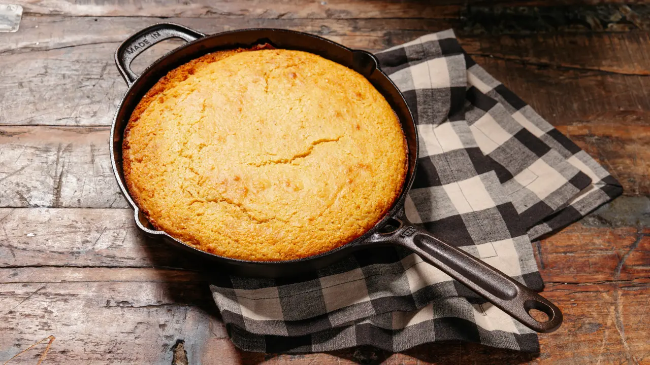 Golden Classic Skillet Cornbread baked in a black cast-iron skillet atop a checkered cloth.