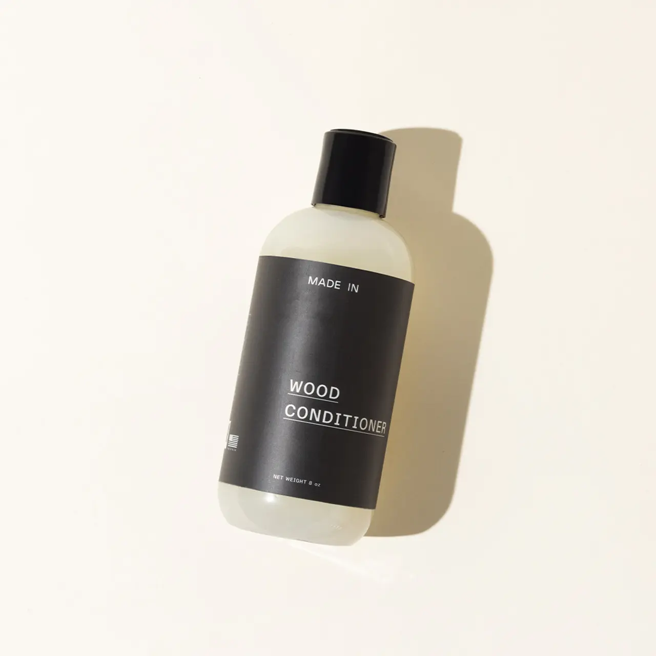 A bottle labeled "WOOD CONDITIONER" is displayed against a simple background, casting a soft shadow.