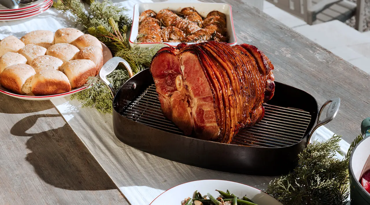 A succulent roasted ham takes center stage on a festive dinner table adorned with various dishes and greenery.