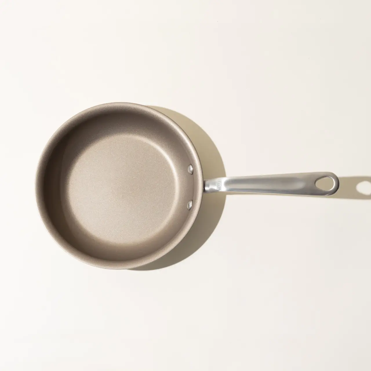 A new non-stick frying pan with a silver handle viewed from above on a light background.