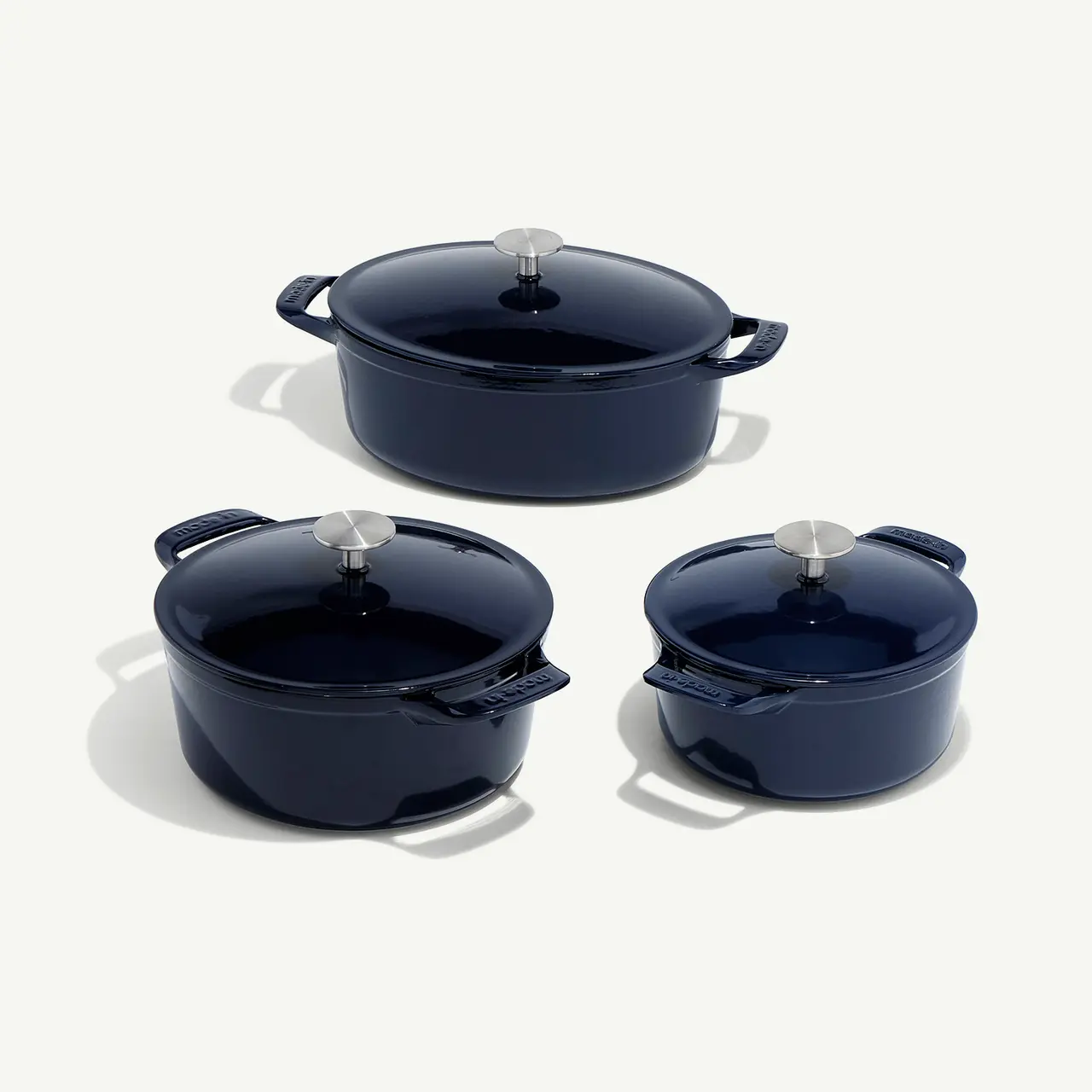 Three navy blue cast iron pots with lids are arranged on a light grey background.