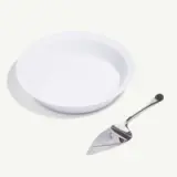 A clean white plate sits next to a polished cake server on a light background.
