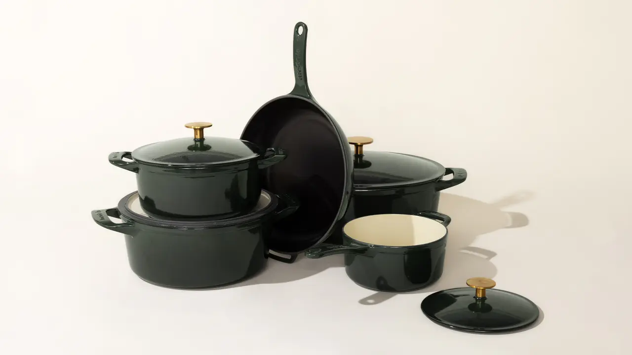 A collection of black cookware with gold-colored handles and lids, including pots, a pan, and a skillet, arranged on a light background.