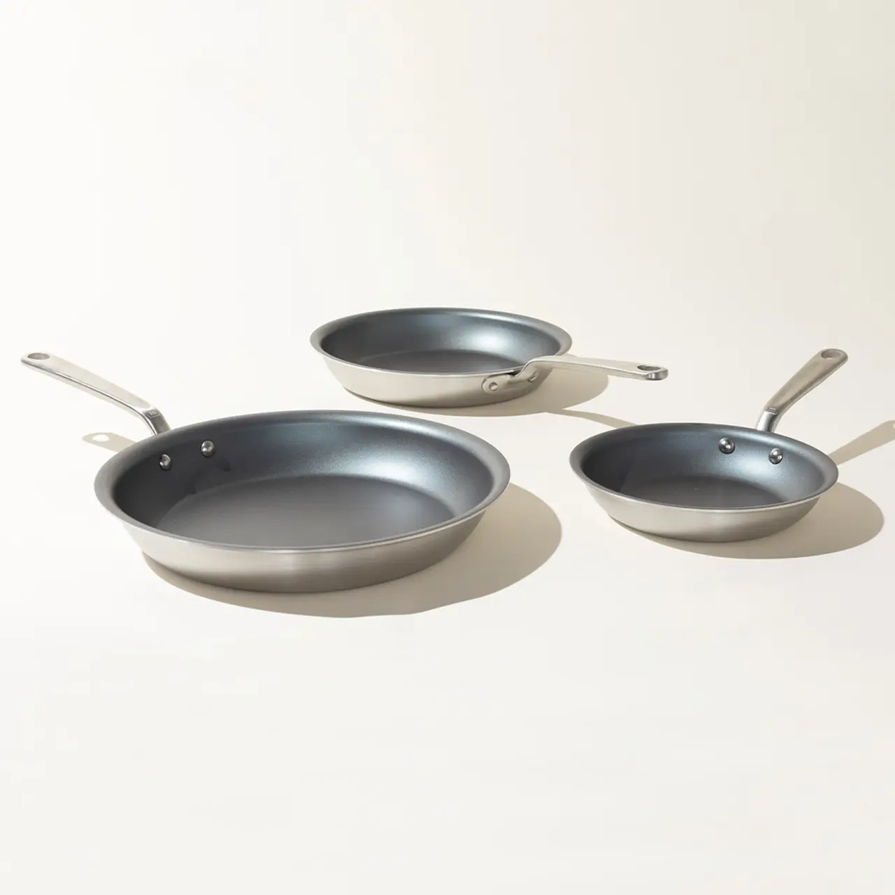 Three different sized non-stick frying pans are arranged in ascending order on a light background.