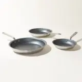 Three different sized non-stick frying pans are arranged in ascending order on a light background.