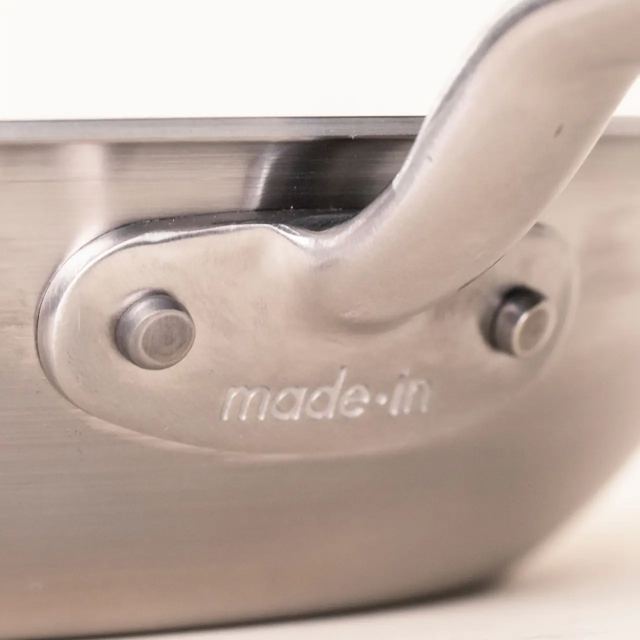 A close-up shows a stainless steel pan's handle riveted to the body with "made.in" engraved on the surface.