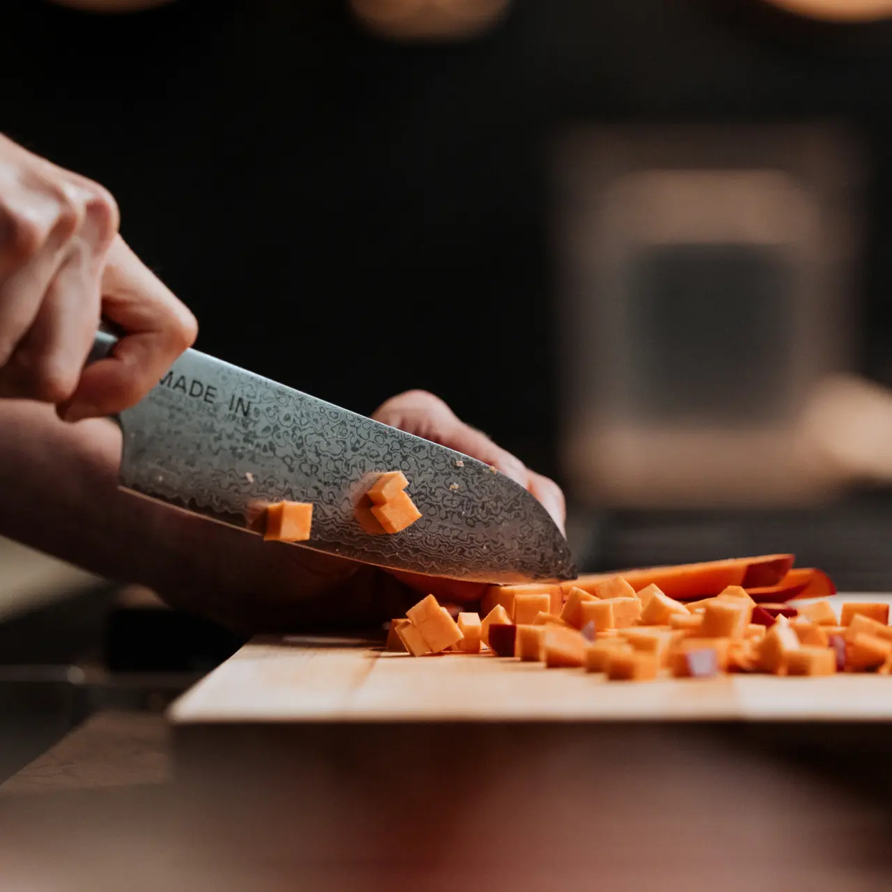 A person is slicing carrots on a wooden cutting board with a large knife.