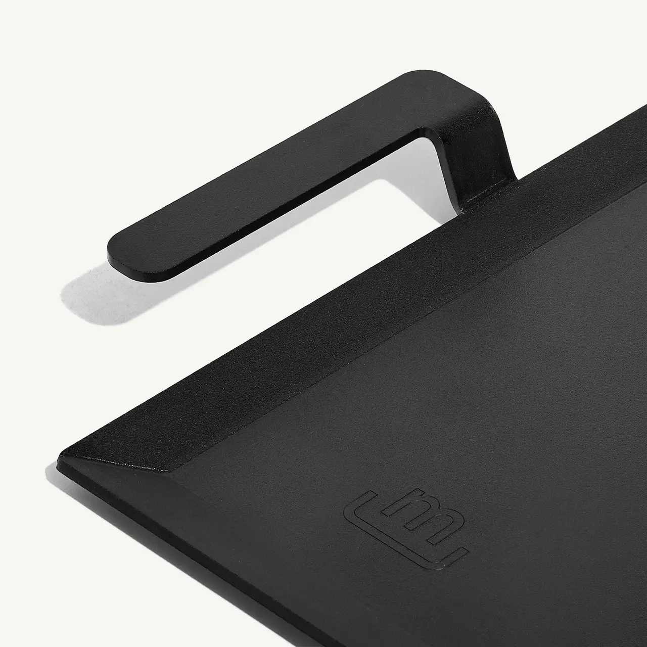 A close-up of a black tablet cover with a stylized logo embossed in the lower right corner and a black loop designed to hold a stylus.