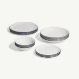 A set of white dishes with blue trim, including plates and bowls, arranged neatly on a light background.