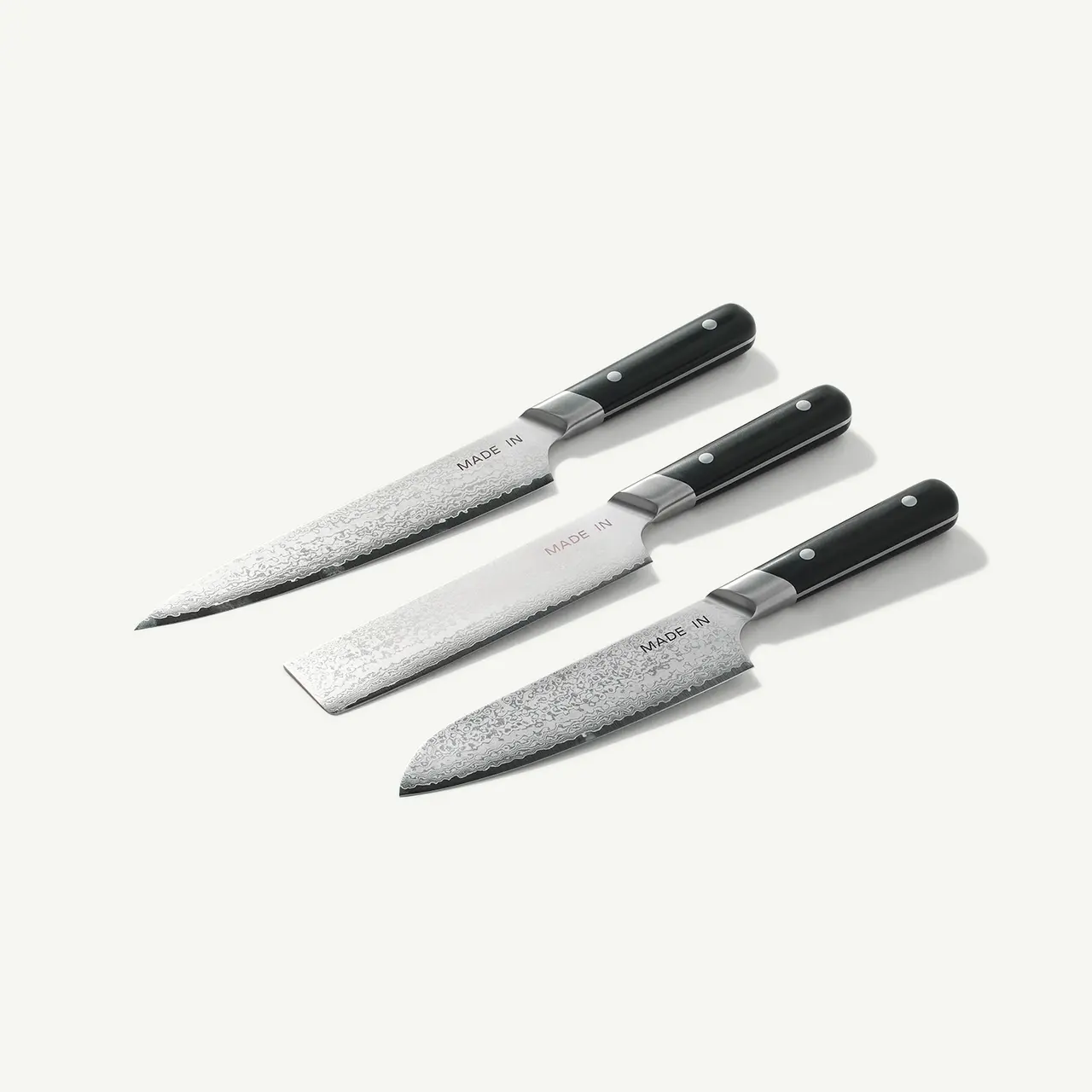 Three chef's knives with black handles are arranged on a light background, displaying their various sizes and blade textures.