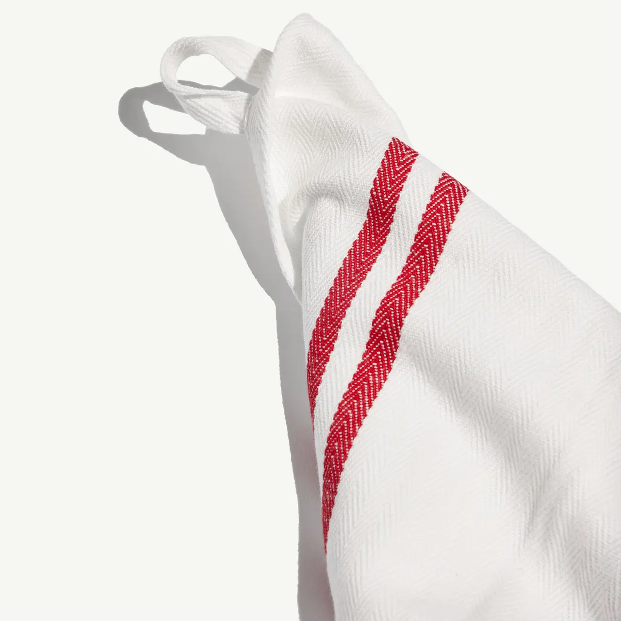 A piece of fabric, possibly a kitchen towel, with two red stripes is draped, casting a shadow on a light surface.