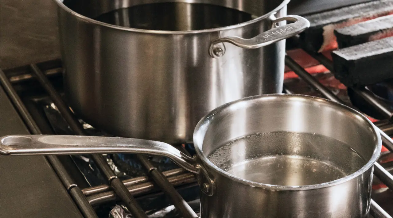 Two stainless steel pots sit on a stove with one containing boiling water.
