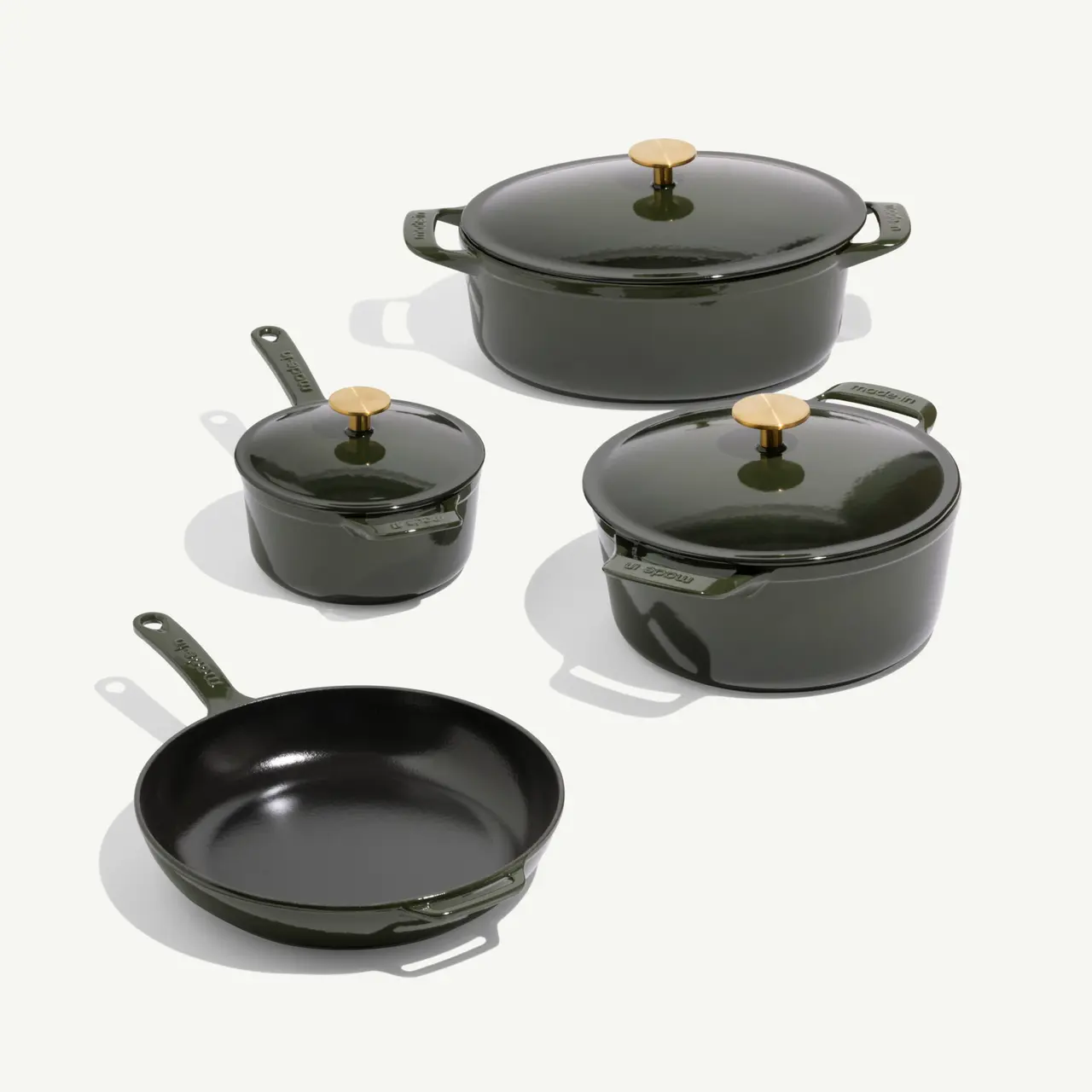 A set of four elegant green cookware pieces, including a shallow dish, two cooking pots with lids, and a frying pan.