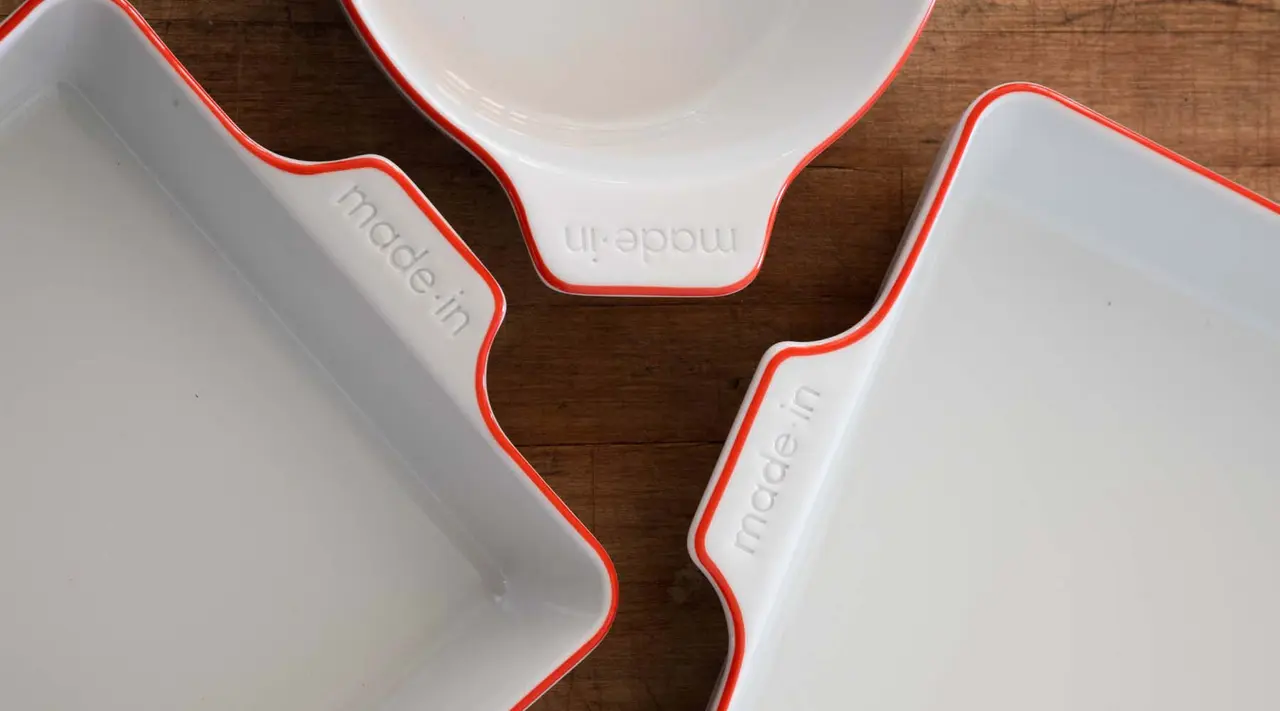 Three white ceramic bakeware dishes with red trim are neatly arranged on a wooden surface.