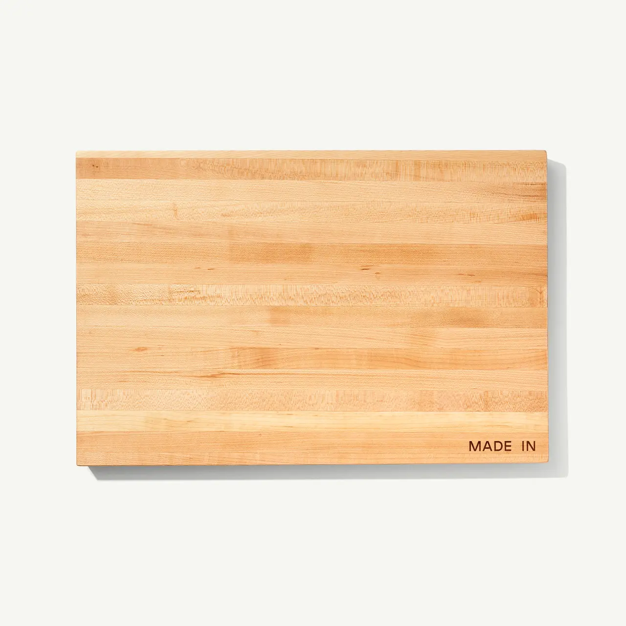 A plain wooden cutting board with visible grain patterns and "MADE IN" text etched in one corner is shown against a white background.