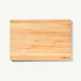 A plain wooden cutting board with visible grain patterns and "MADE IN" text etched in one corner is shown against a white background.