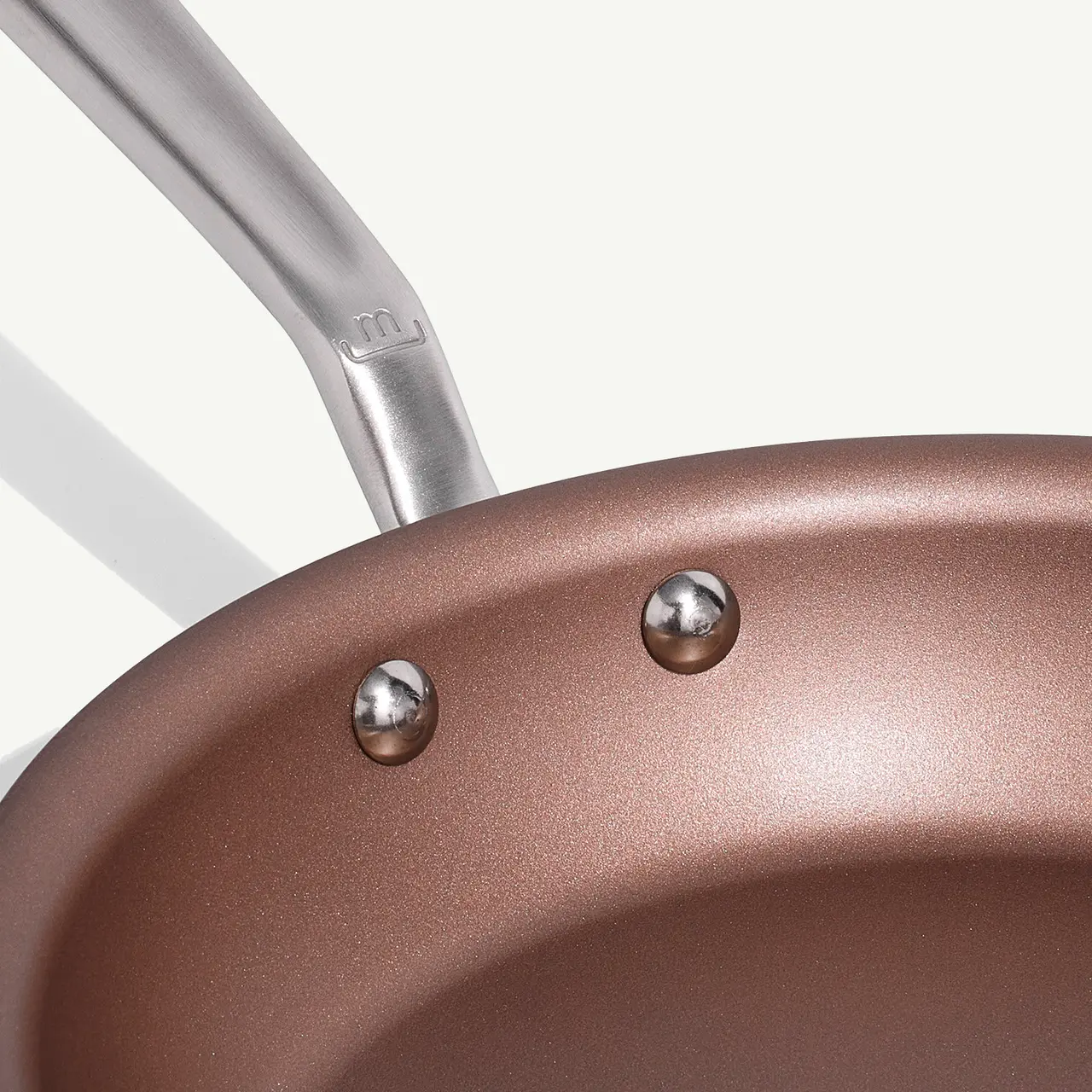 A close-up view of a non-stick frying pan with two rivets attaching the handle to the body.