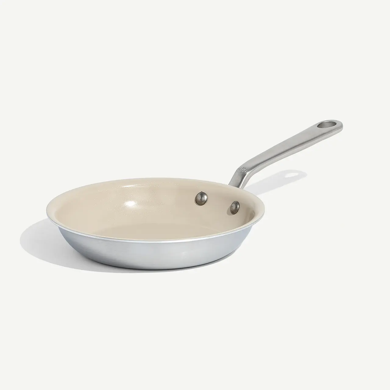 A non-stick frying pan with a silver handle sits isolated on a light background.