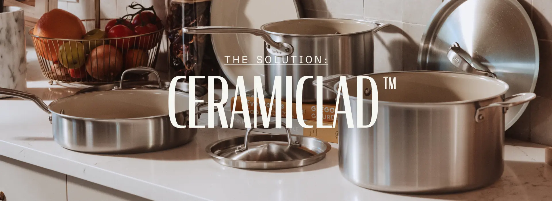 A collection of stainless steel cookware is displayed on a countertop, accompanied by a text overlay promoting "Ceramiclad™."