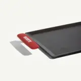 A black griddle with a red handle and a spatula rests beside it.