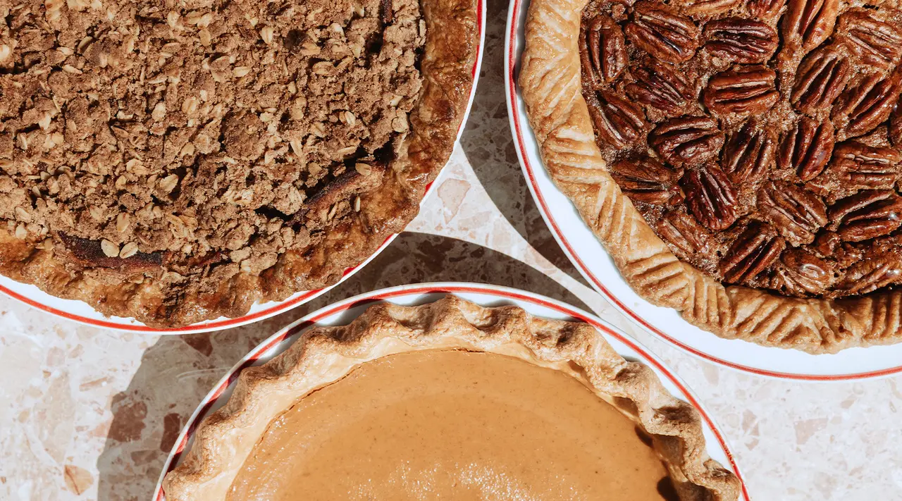 Three different pies, possibly with toppings of nuts and streusel, are arranged on a surface.