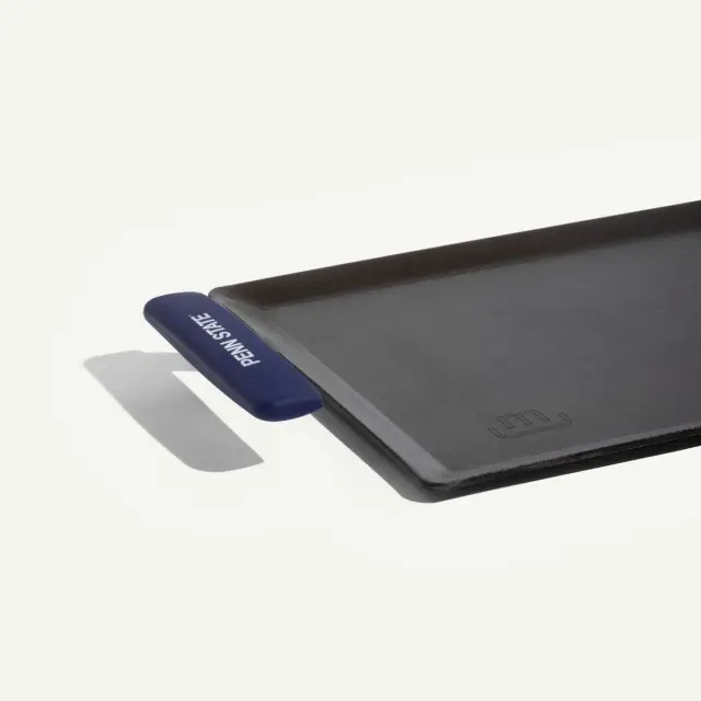 A rectangular, black baking sheet with a blue silicone handle on one side is displayed against a light background.