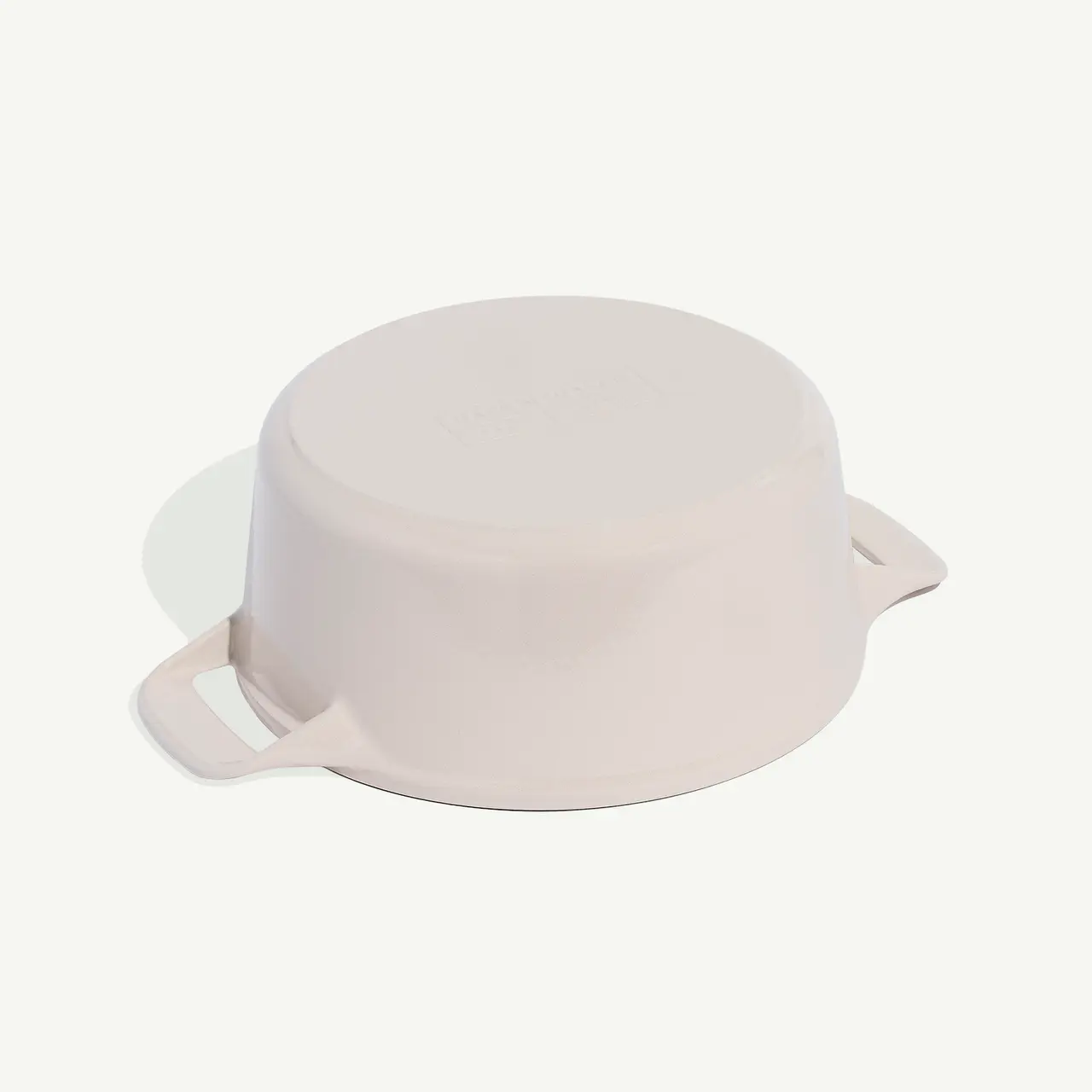 A pale pink ceramic pot with handles and a visible brand name on the lid, isolated against a white background.