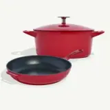 A red cast iron Dutch oven with a lid next to a matching skillet on a white background.