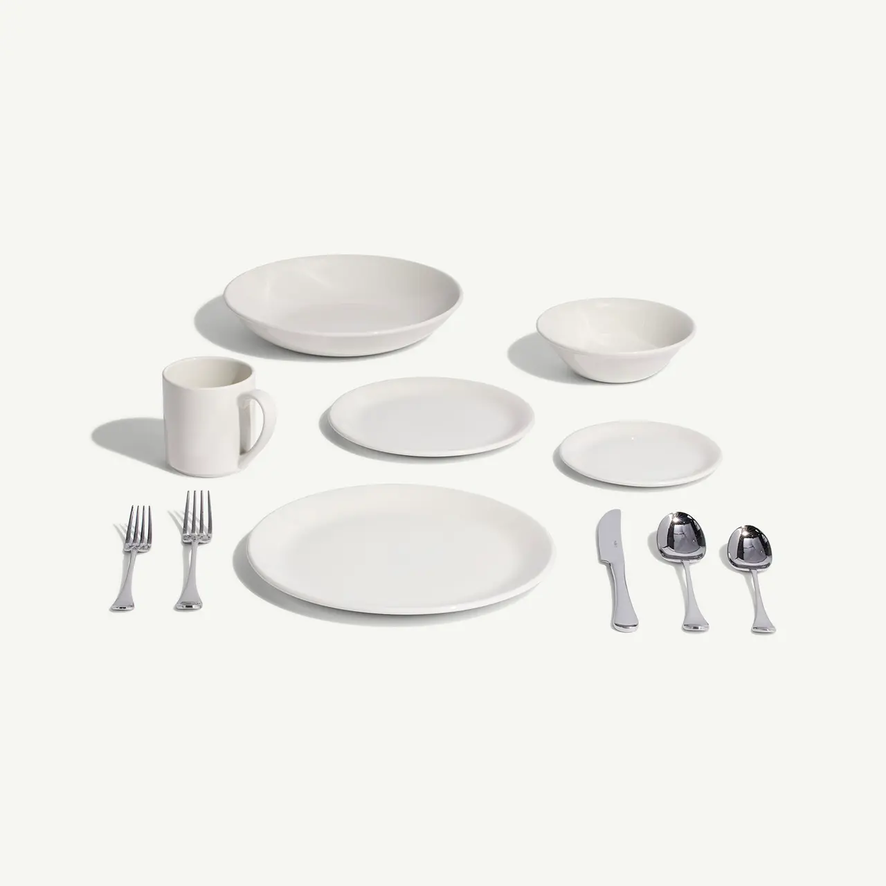 A neatly arranged set of white dinnerware and silverware against a light background.